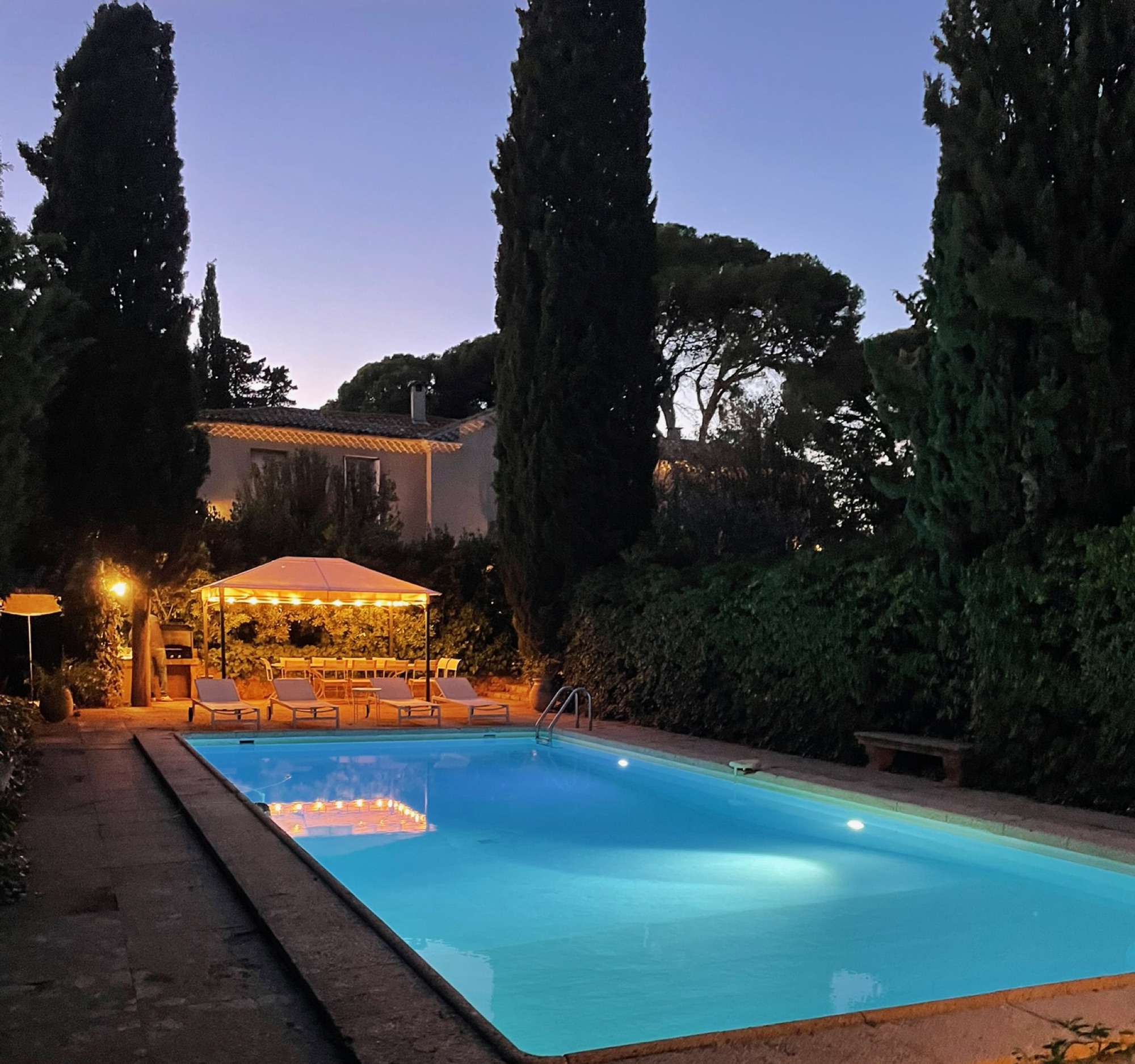 La piscine au crépuscule, éclairée entre les cyprès